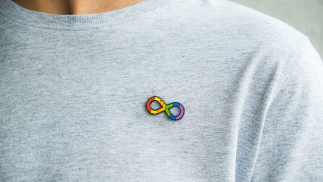 Person wearing a grey tshirt with a neurodiversity infinity logo pin badge