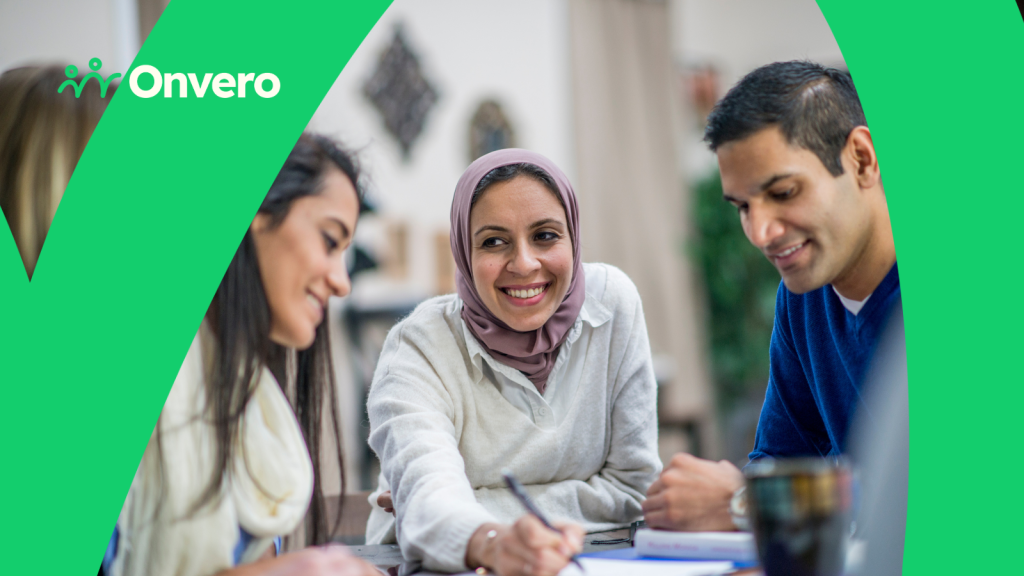 The image depicts a group of three people engaged in conversation at a table. A woman in the centre, wearing a light purple hijab, smiles as she writes on a piece of paper. To her left, a woman is focused on the conversation. To her right, a man is also participating. In the top left corner, in white text, reads "Employee Network Hub." The bottom right corner displays the Onvero logo.