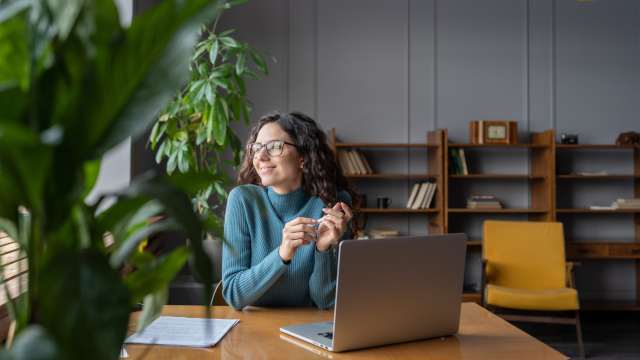 The image features a woman sitting at a desk, looking to her left with a serene smile. In front of her is an open laptop and a sheet of paper with some text on it. A large green leaf is visible in the foreground on the left, partially out of focus, which adds depth to the peaceful scene. The Onvero logo is displayed in the bottom right corner.